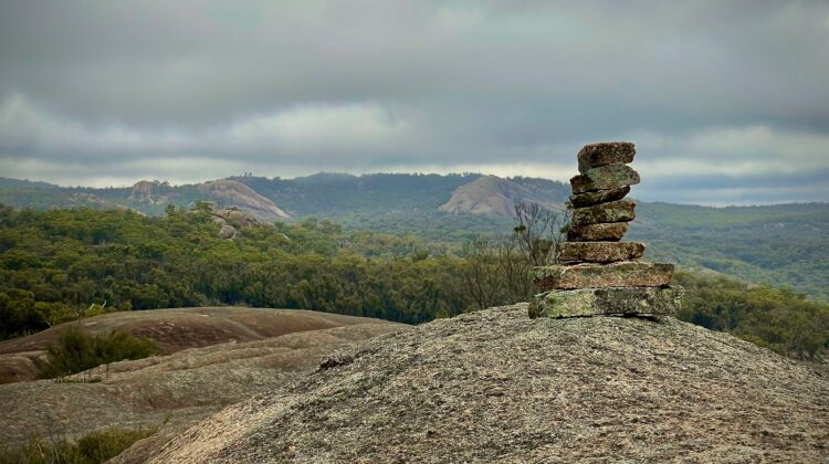 A small stack of balanced stones on a granite outcrop overlooking hills