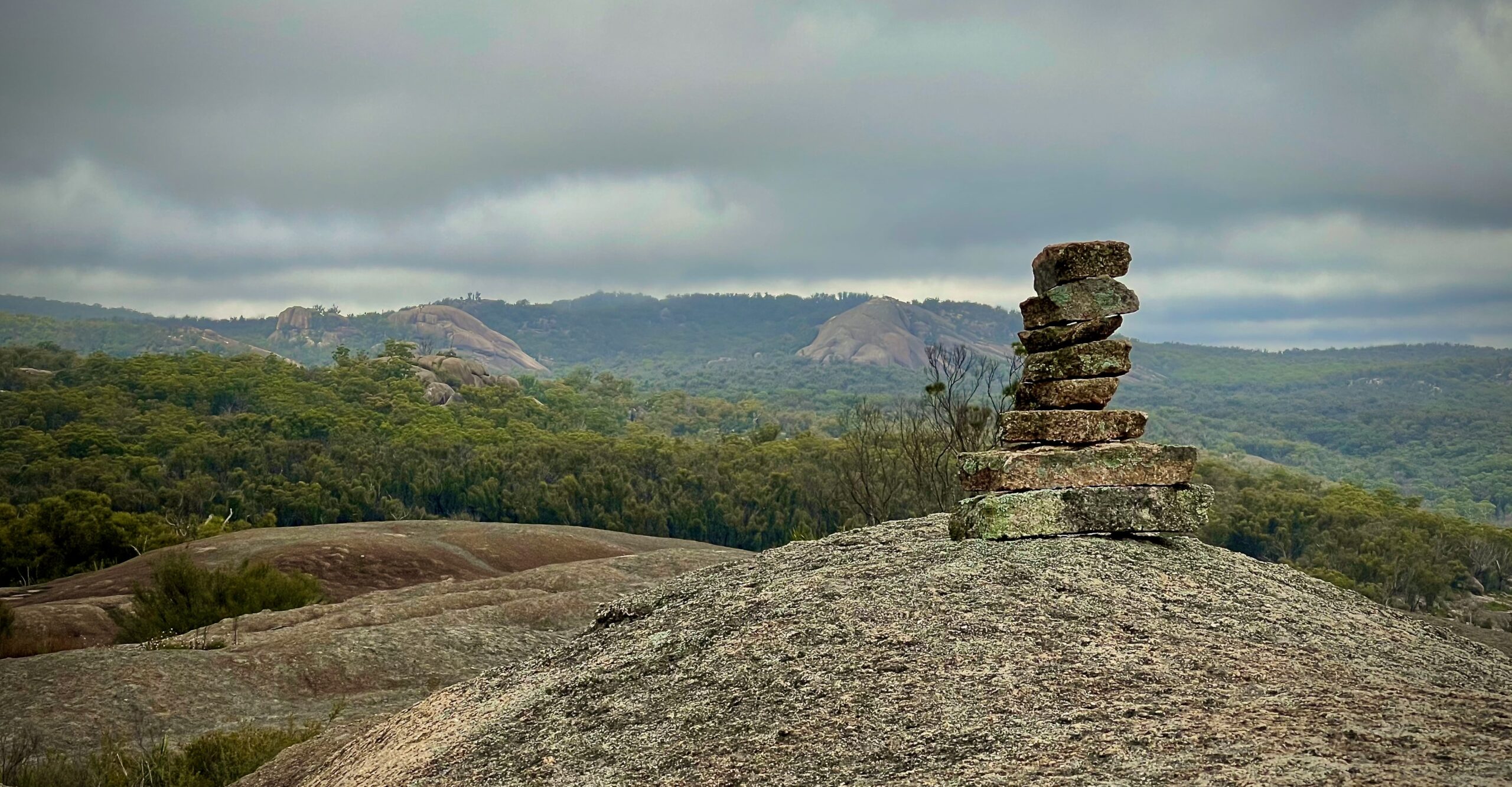 A small stack of balanced stones on a granite outcrop overlooking hills