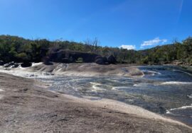 Creek water flowing across a broad granite slab under a blue sky