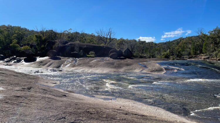 Creek water flowing across a broad granite slab under a blue sky