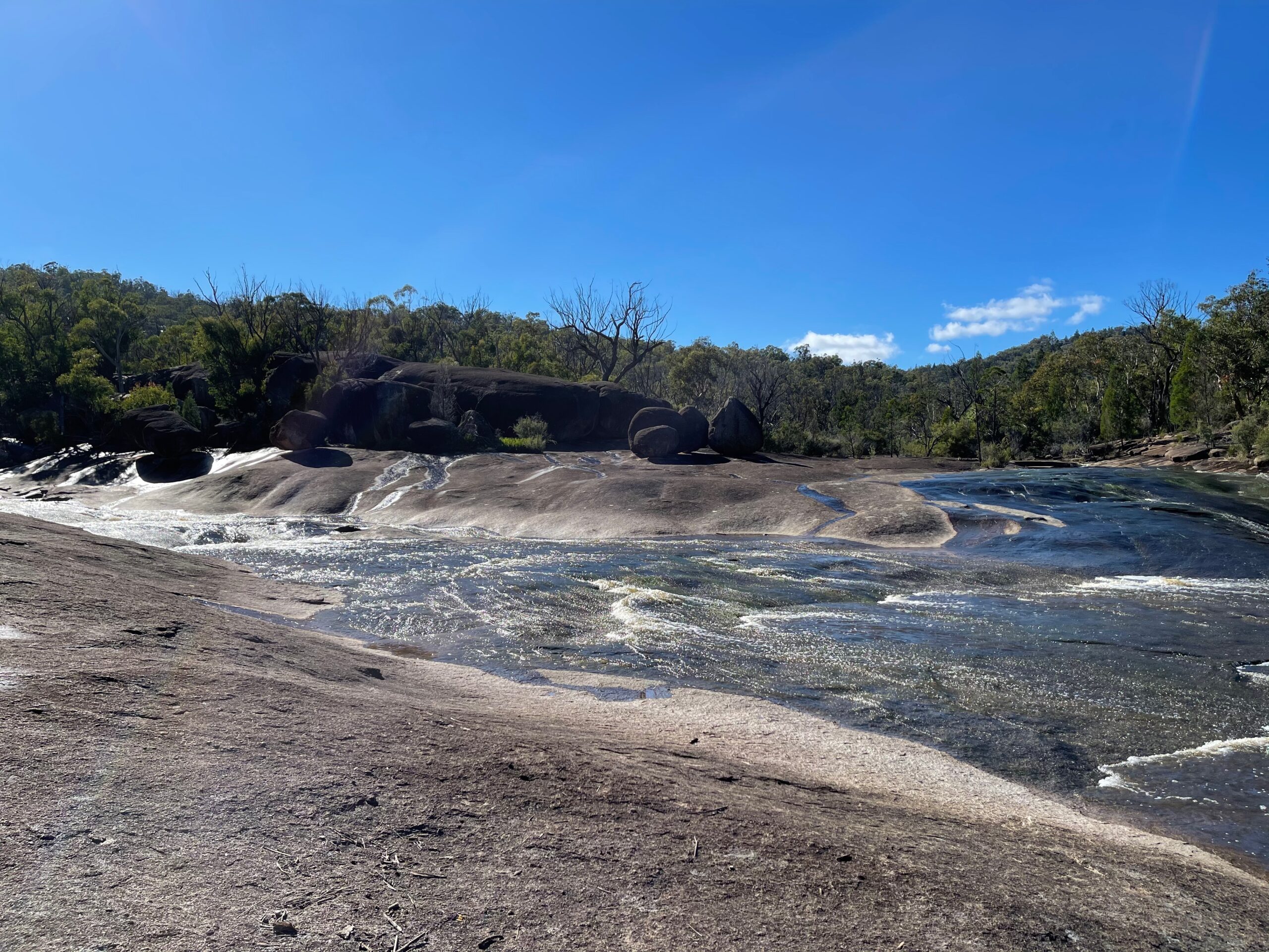 Creek water flowing across a broad granite slab under a blue sky