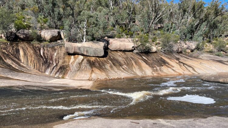 Water running over banded granite rock beside bushland