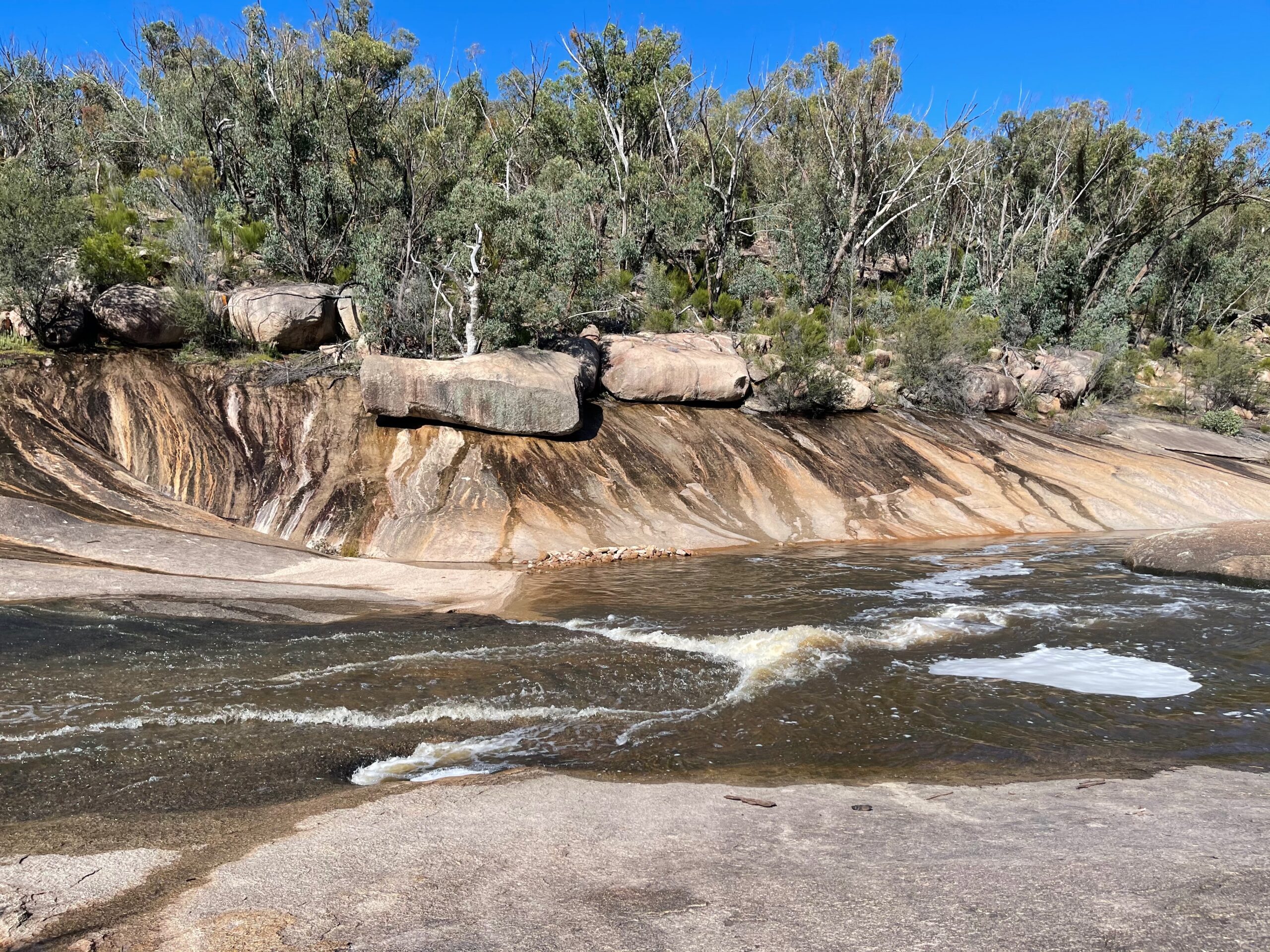 Water running over banded granite rock beside bushland